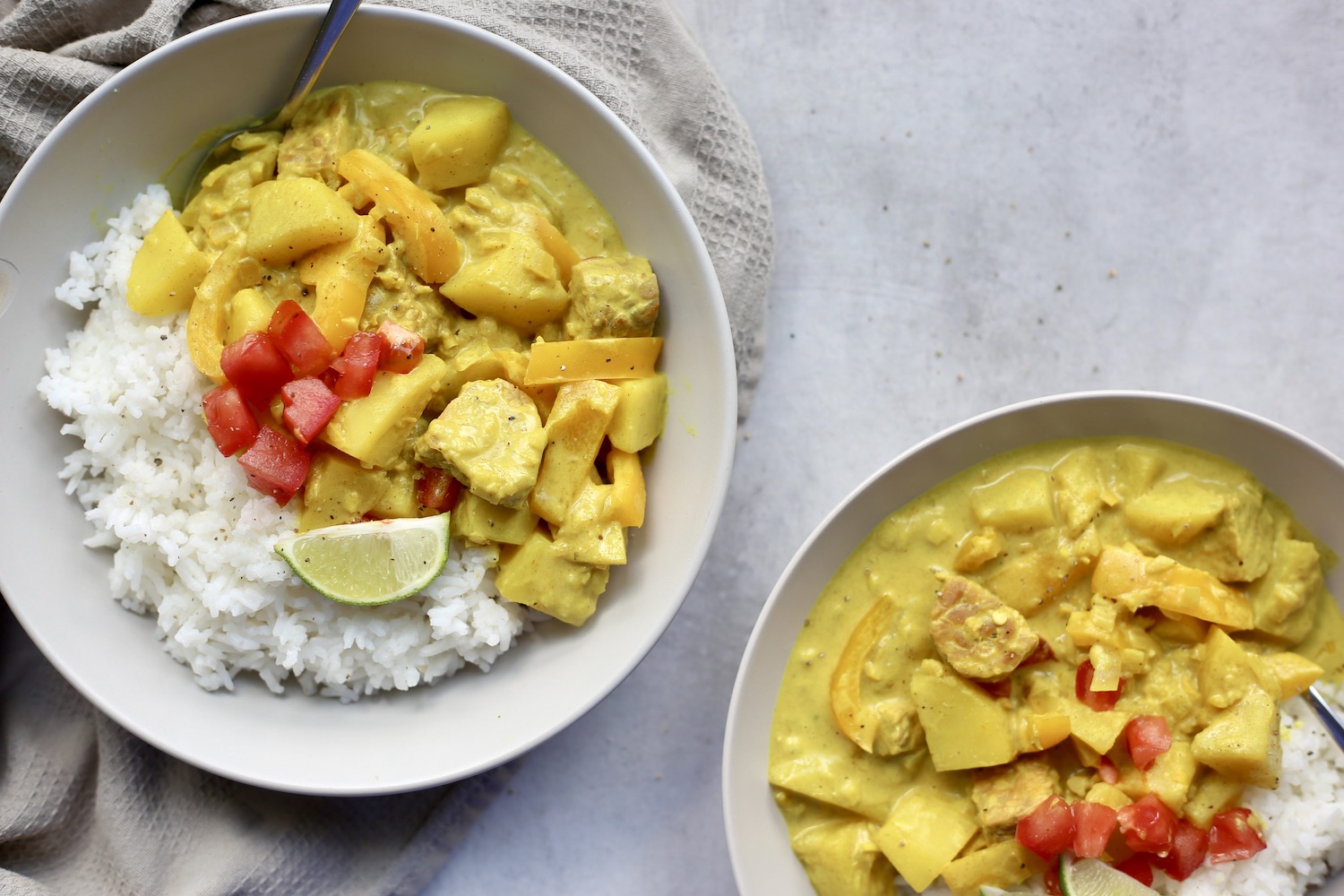 an above shot of two bowls full of vegan massaman curry served with white rice and chopped tomatoes