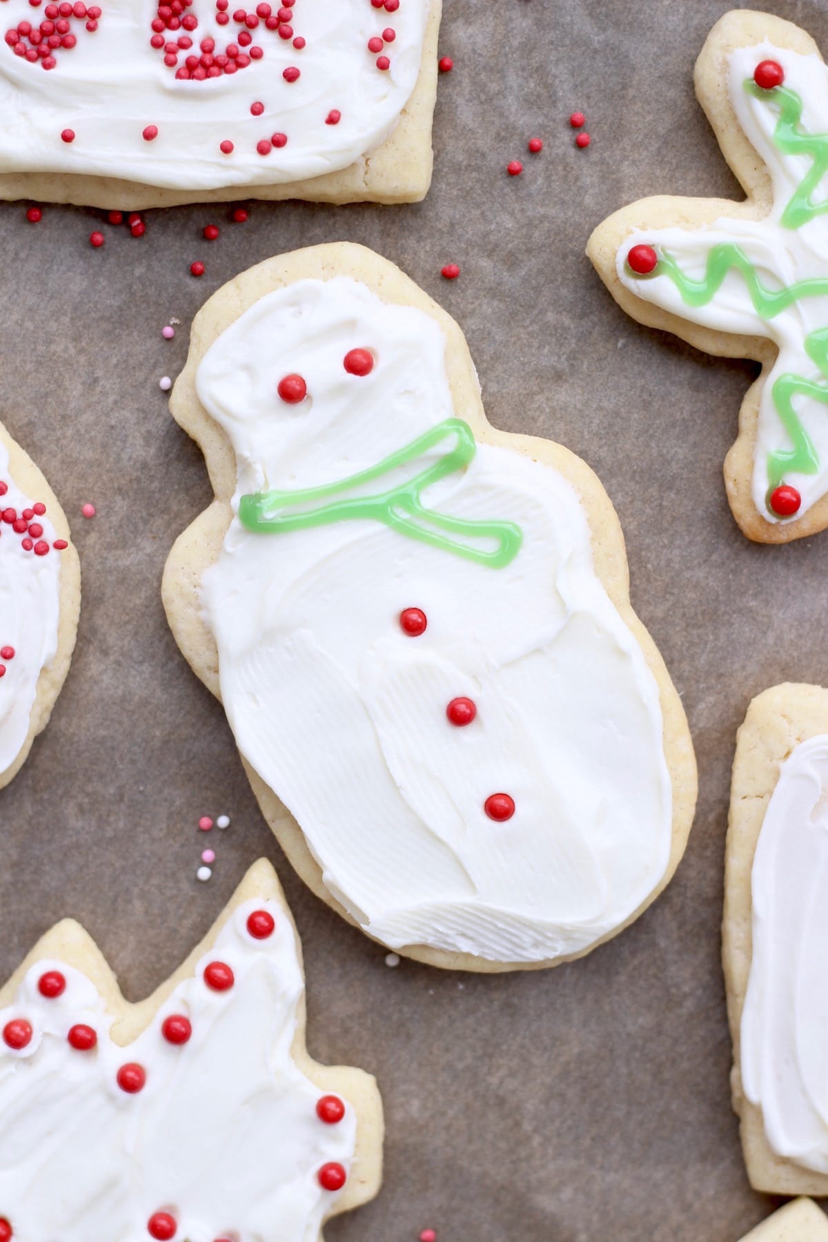 An overhead shot of a vegan sugar cookie cut into the shape of a snowman and decorated with white icing and red sprinkles. 