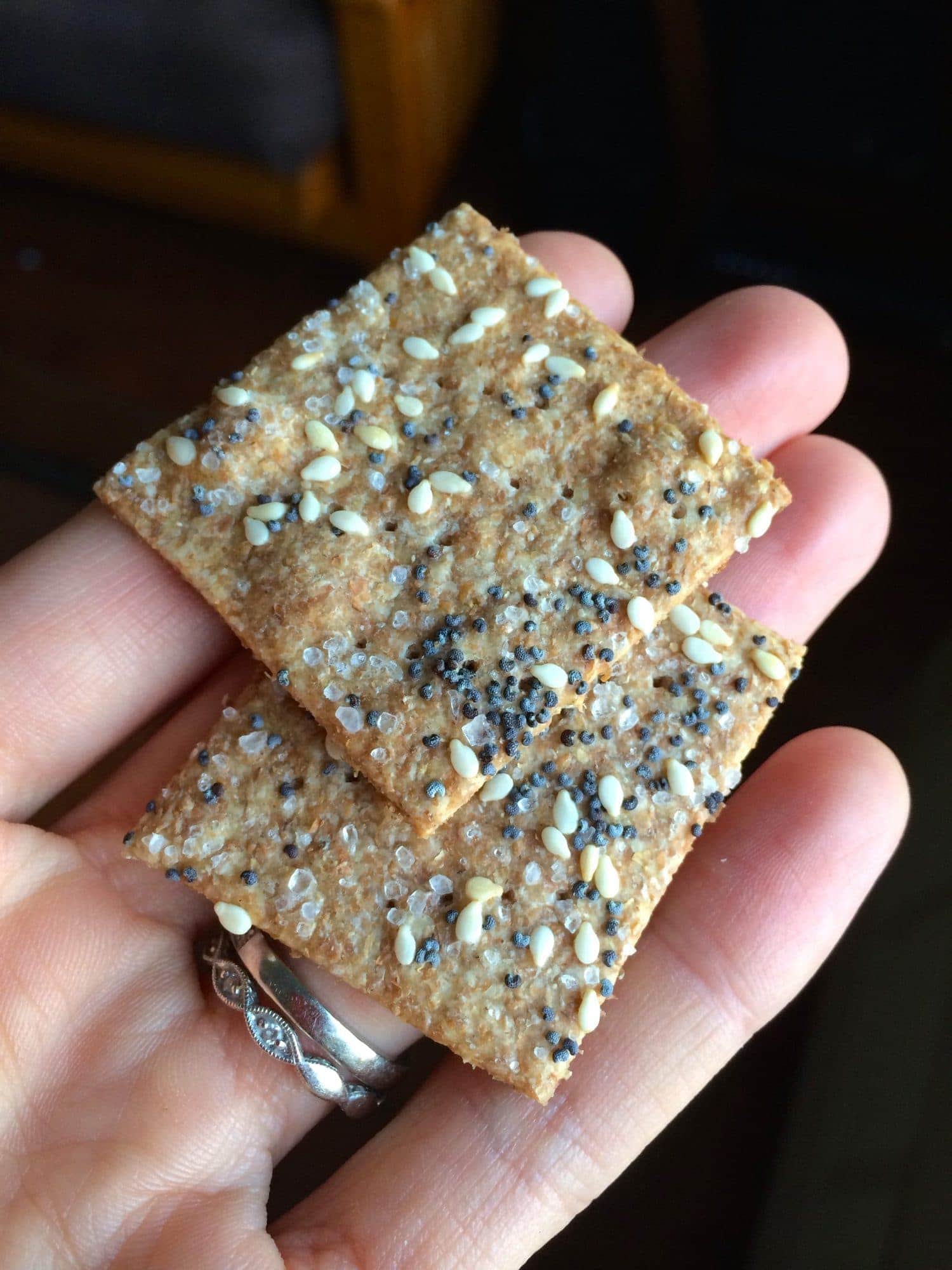 A hand holding two sesame seed whole wheat crackers. 