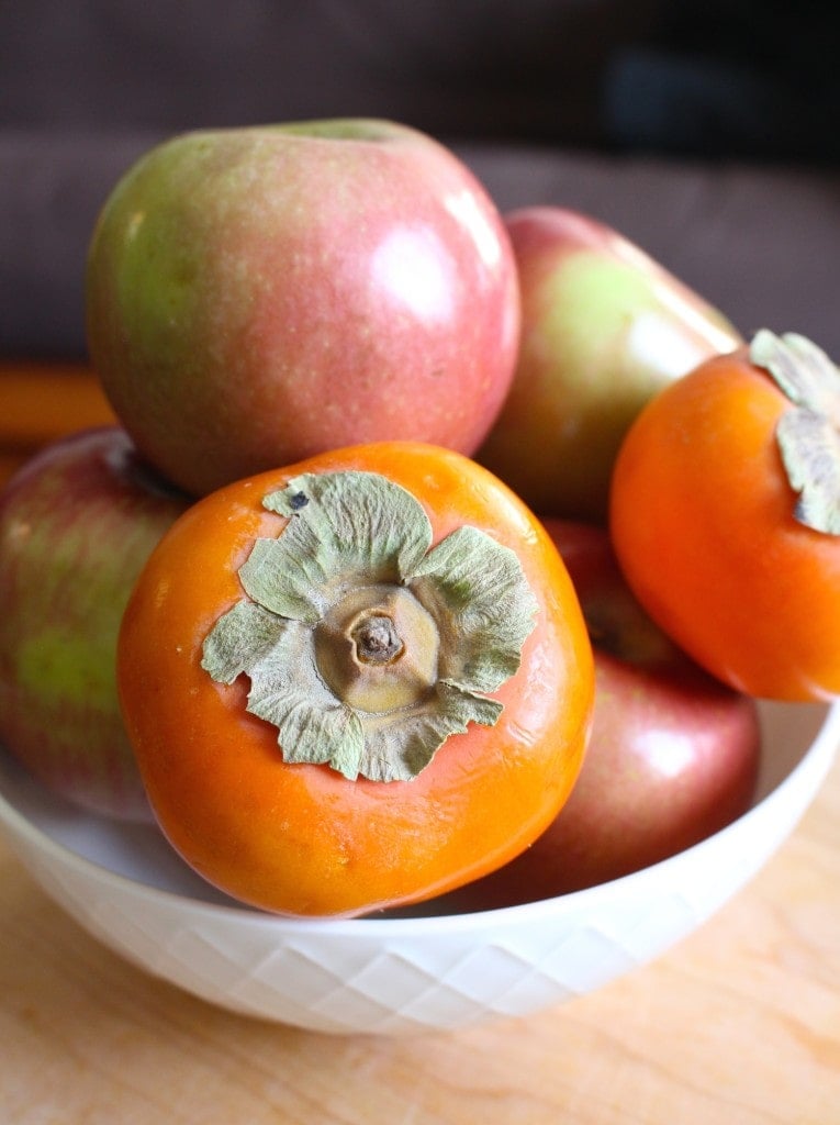 Persimmons and apples piled high in a bowl