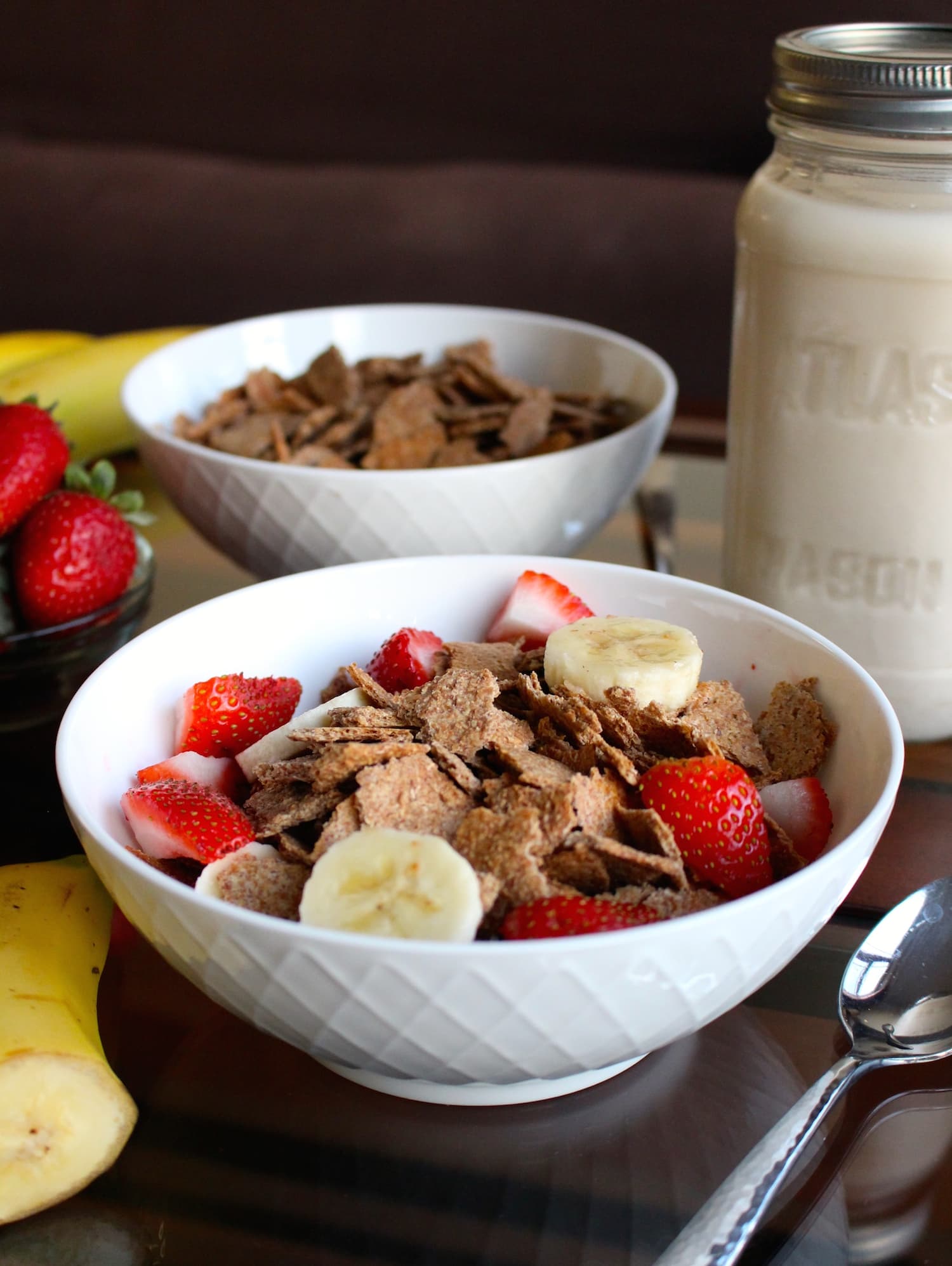 Two write bowls full of Homemade Bran Flakes Cereal topped with banana and strawberries. 