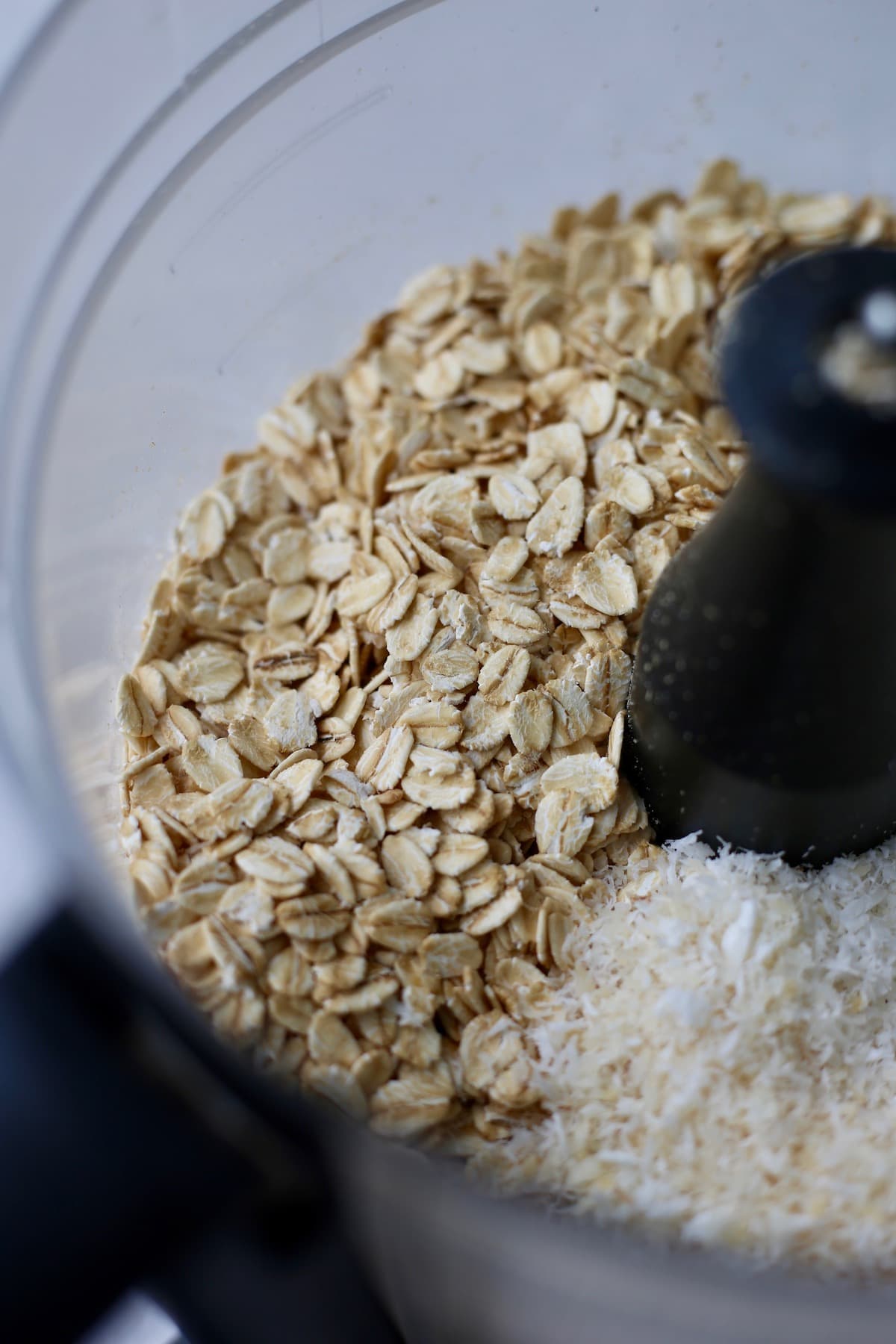 Rolled oats and desiccated coconut in the bowl of a food processor.