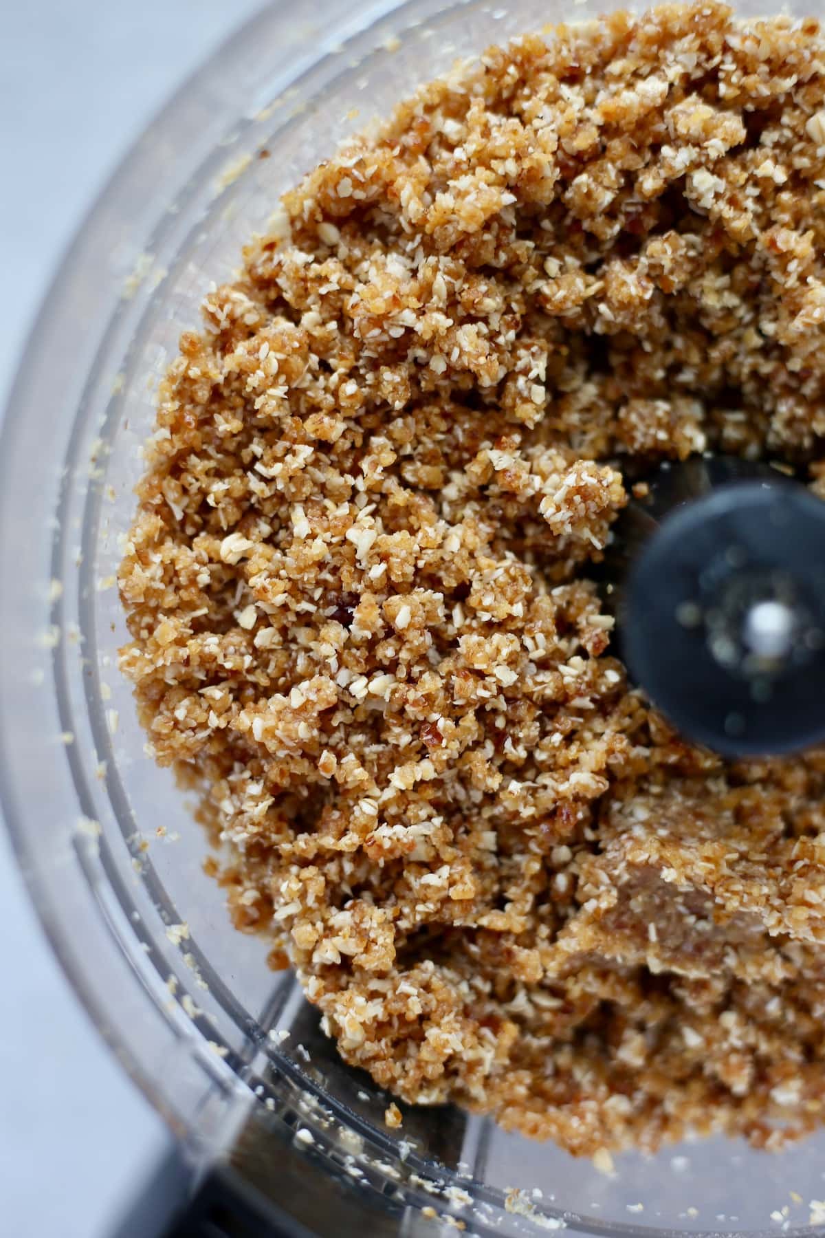 an overhead shot of a crumbly mixture of oats, dates and coconut in the inside of a food processor