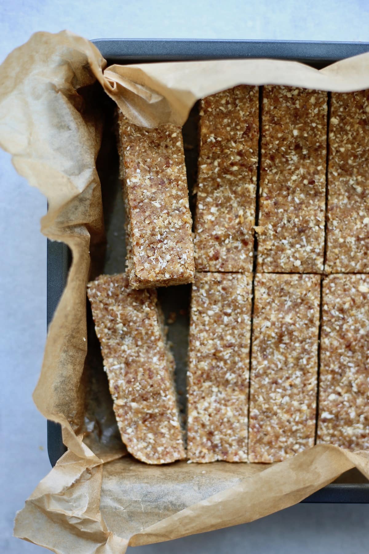 Homemade granola bars cut into rectangles in a baking dish lined with brown parchment paper.