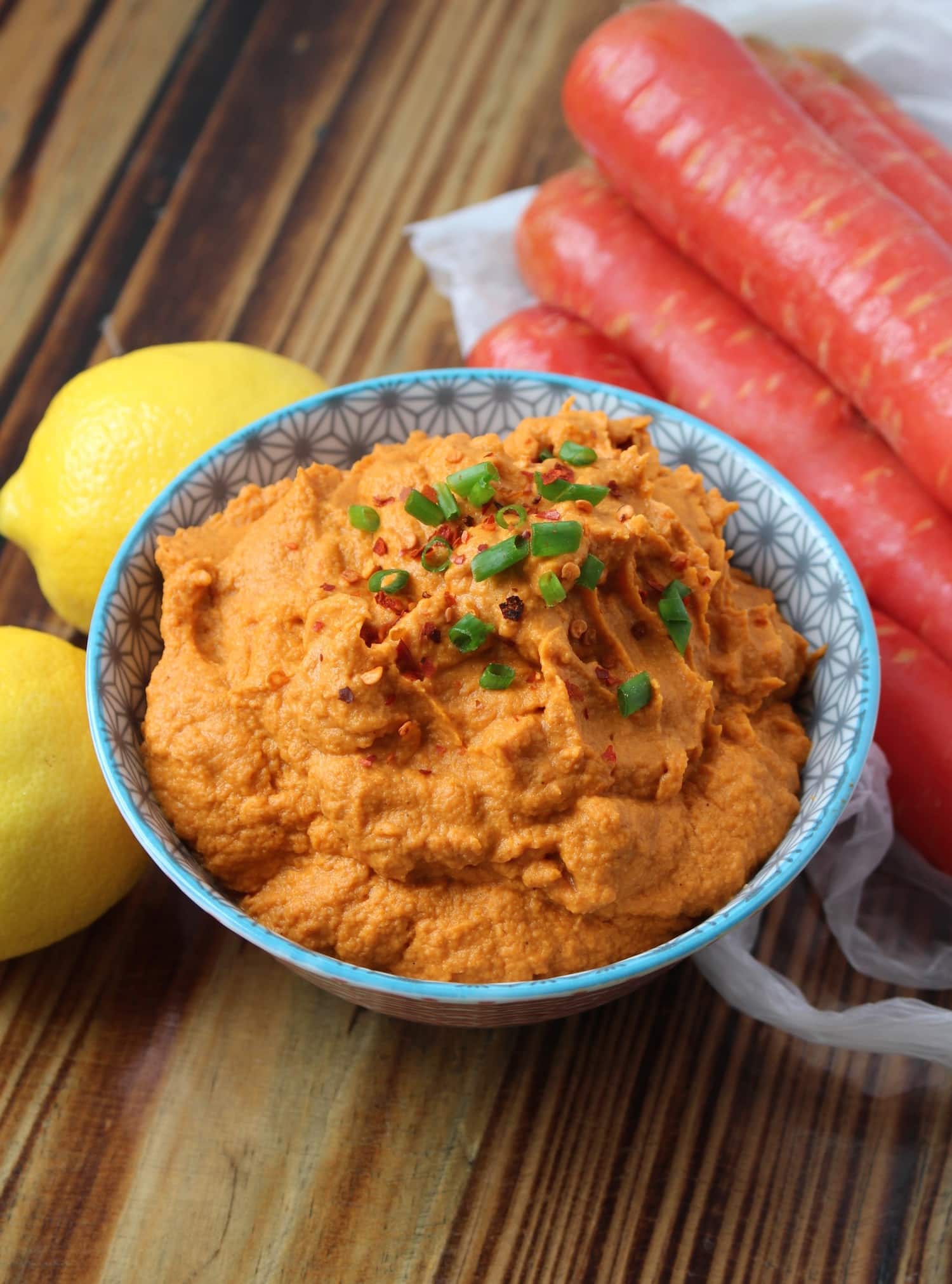 beanless carrot hummus in a bowl on the table next to carrots and lemons