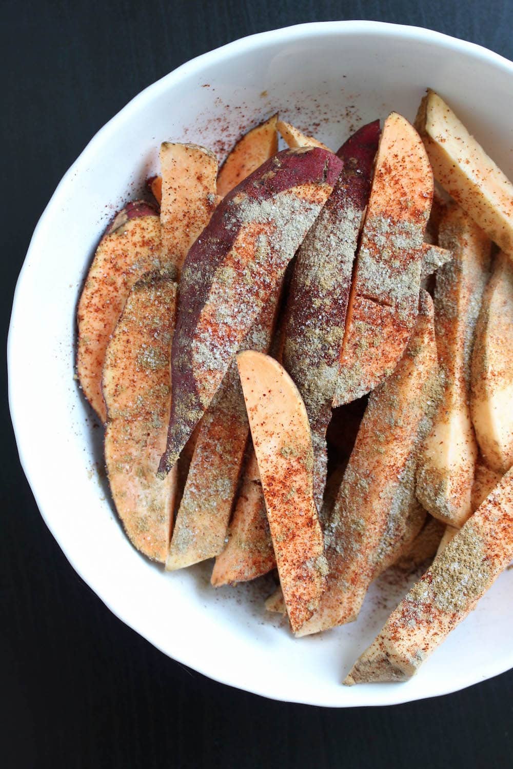 sweet potato fries being coated in spices in a mixing bowl
