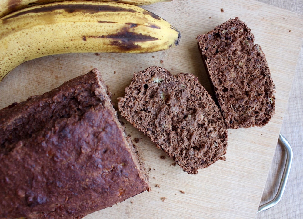 sliced Gluten Free Double Chocolate Banana Bread with banana fruit on the side on a chopping board