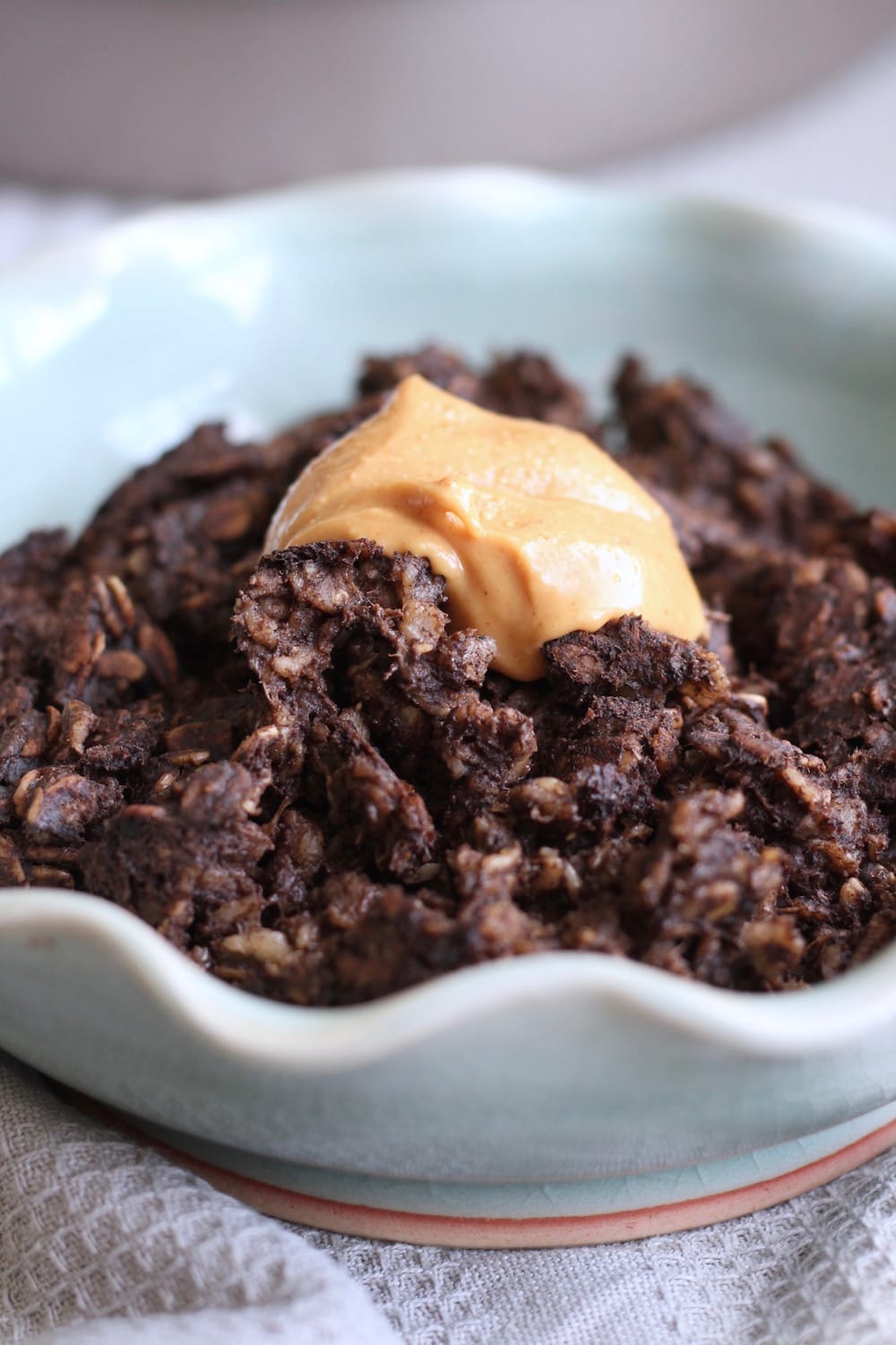 A blue bowl full of chocolate baked oatmeal topped with orange peanut butter.