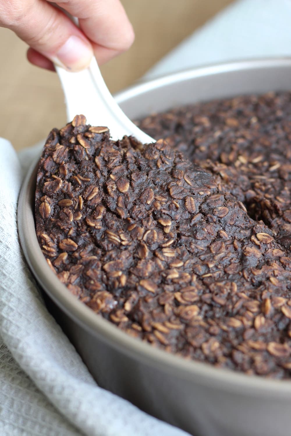 Chocolate baked oatmeal being scooped out of a pan with a white spoon.