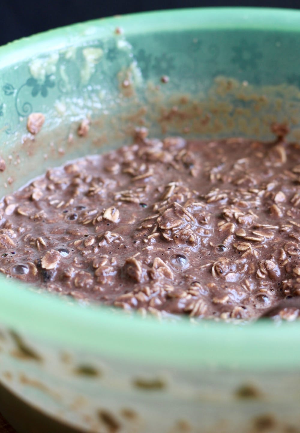 A green mixing bowl filled with a chocolate oatmeal batter.