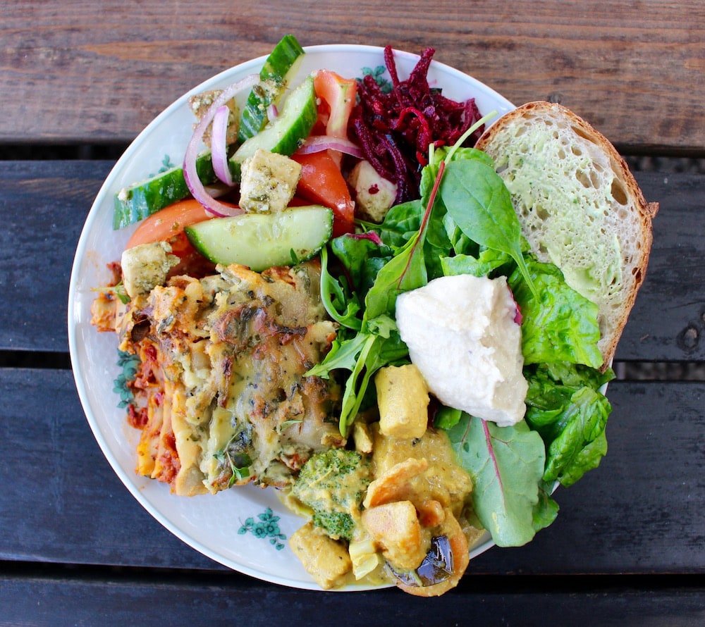 a plateful of lasagna, curry, different spreads with bread, and a variety of salads