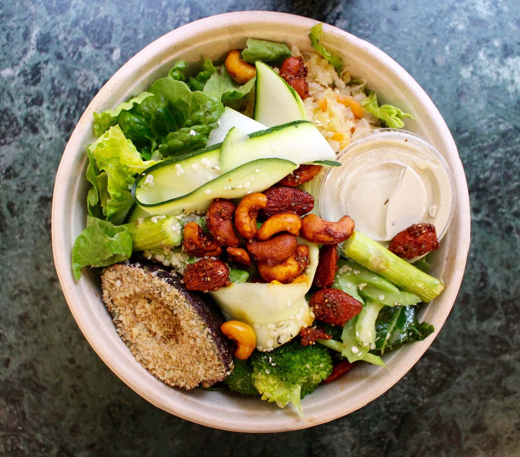 a meal bowl with salad, nuts and dressing