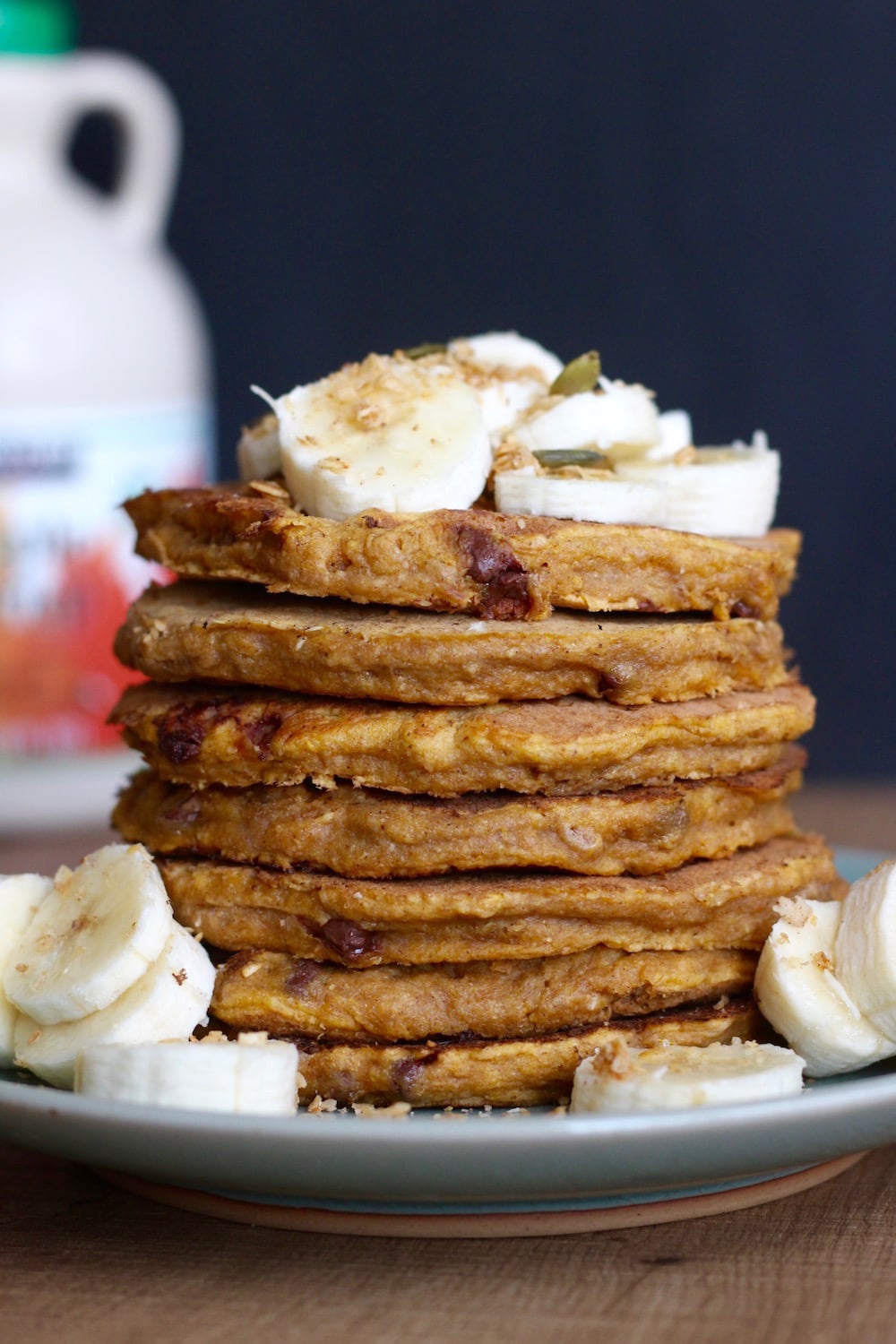 stacked Whole Wheat Vegan Pumpkin Pancakes on plate with sliced bananas on top