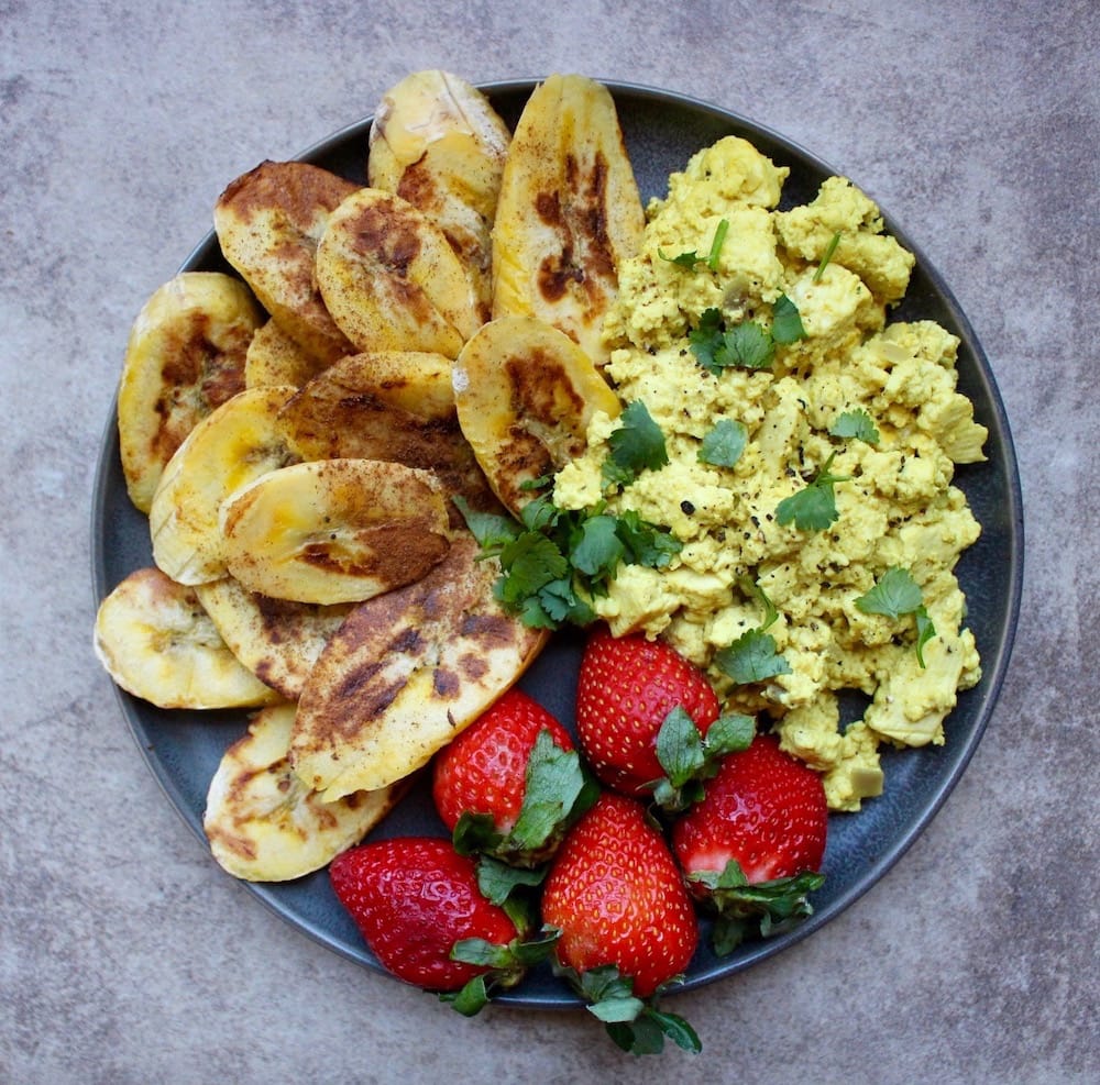 top view of cheesy vegan tofu scramble on a plate with cilantro and strawberries and plantains on the side