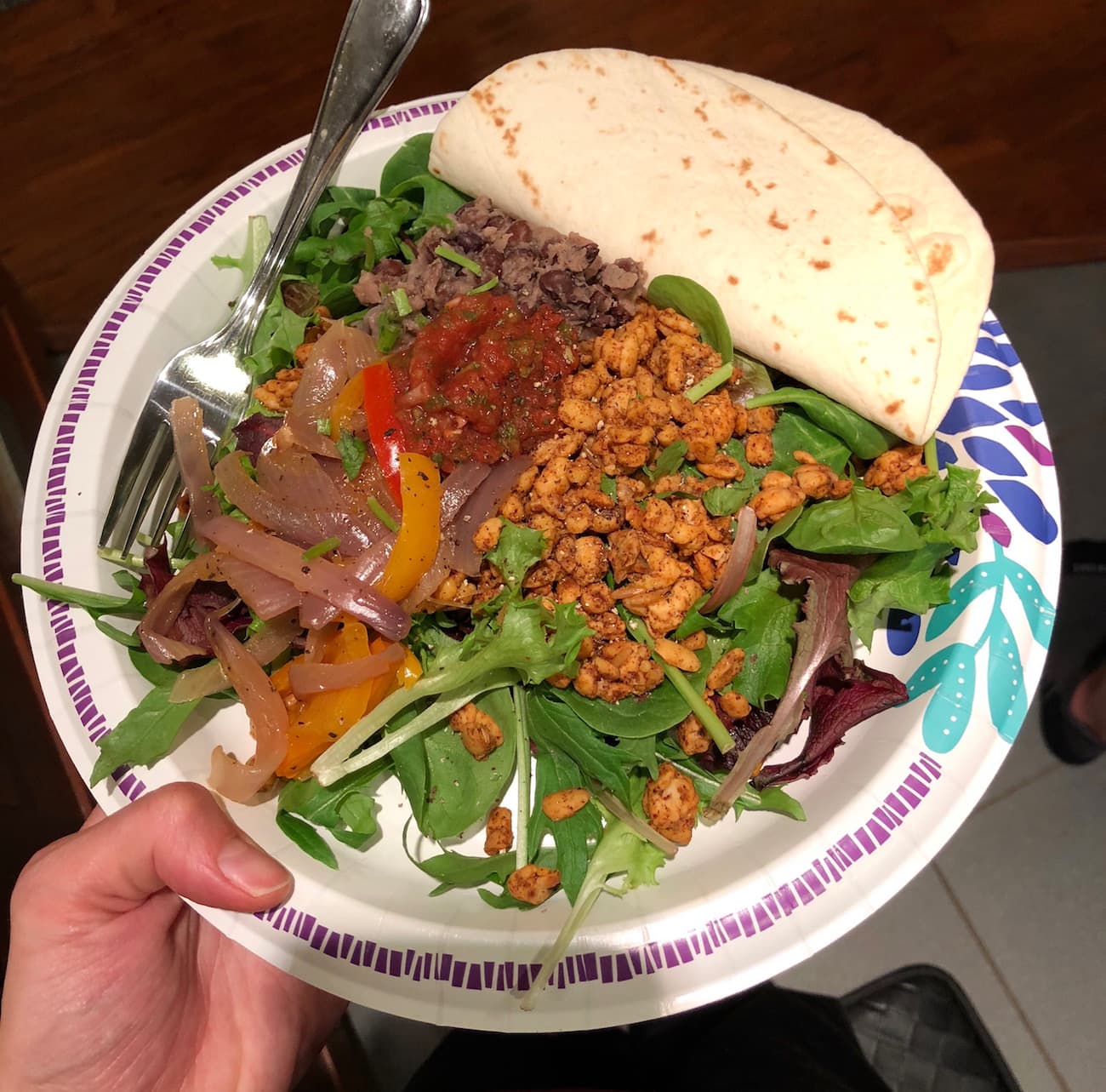 Leftover taco salad topped with tempeh, beans, veggies and salsa with a flour tortilla