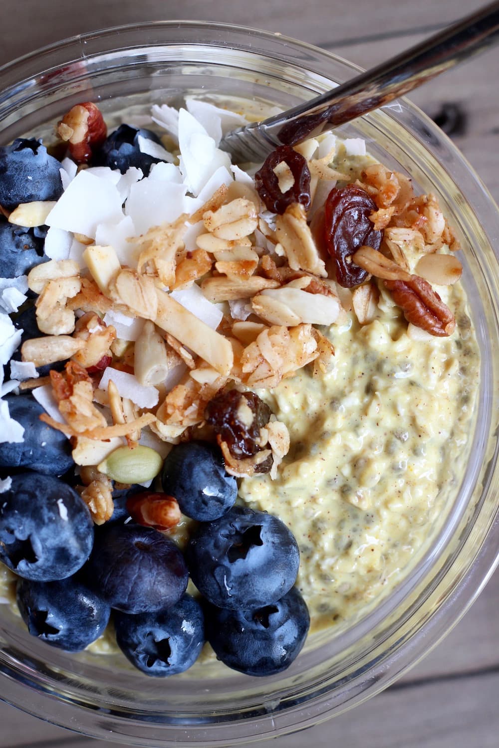 Vegan Golden Milk Overnight Oats in a bowl topped with nuts, raisins and blueberries top view