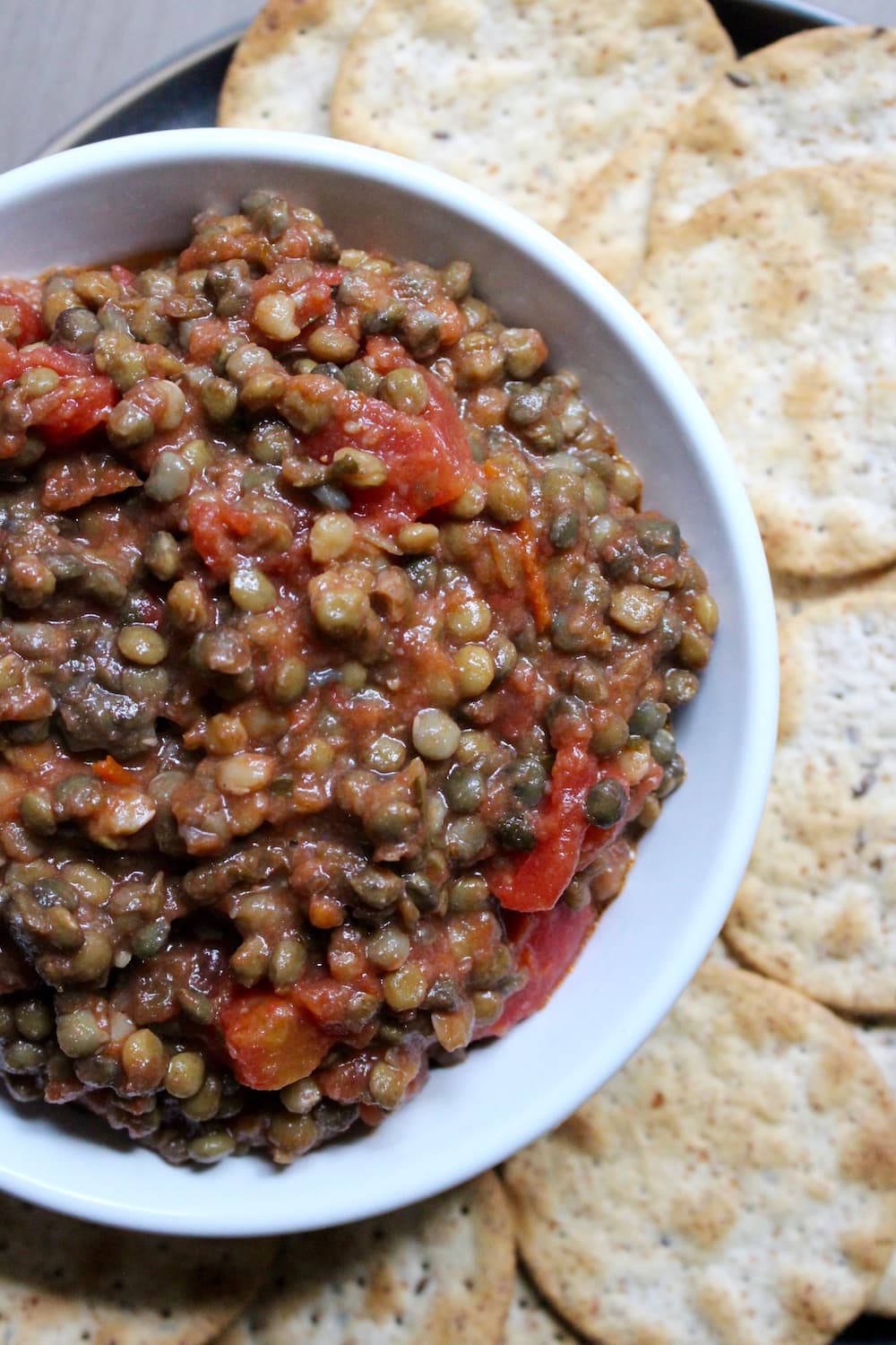 lentil bruschetta dip in a bowl surrounded by crackers