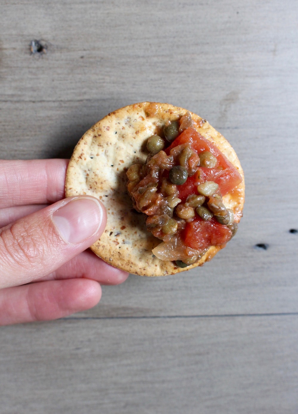 lentil bruschetta dip on a cracker being help by a hand