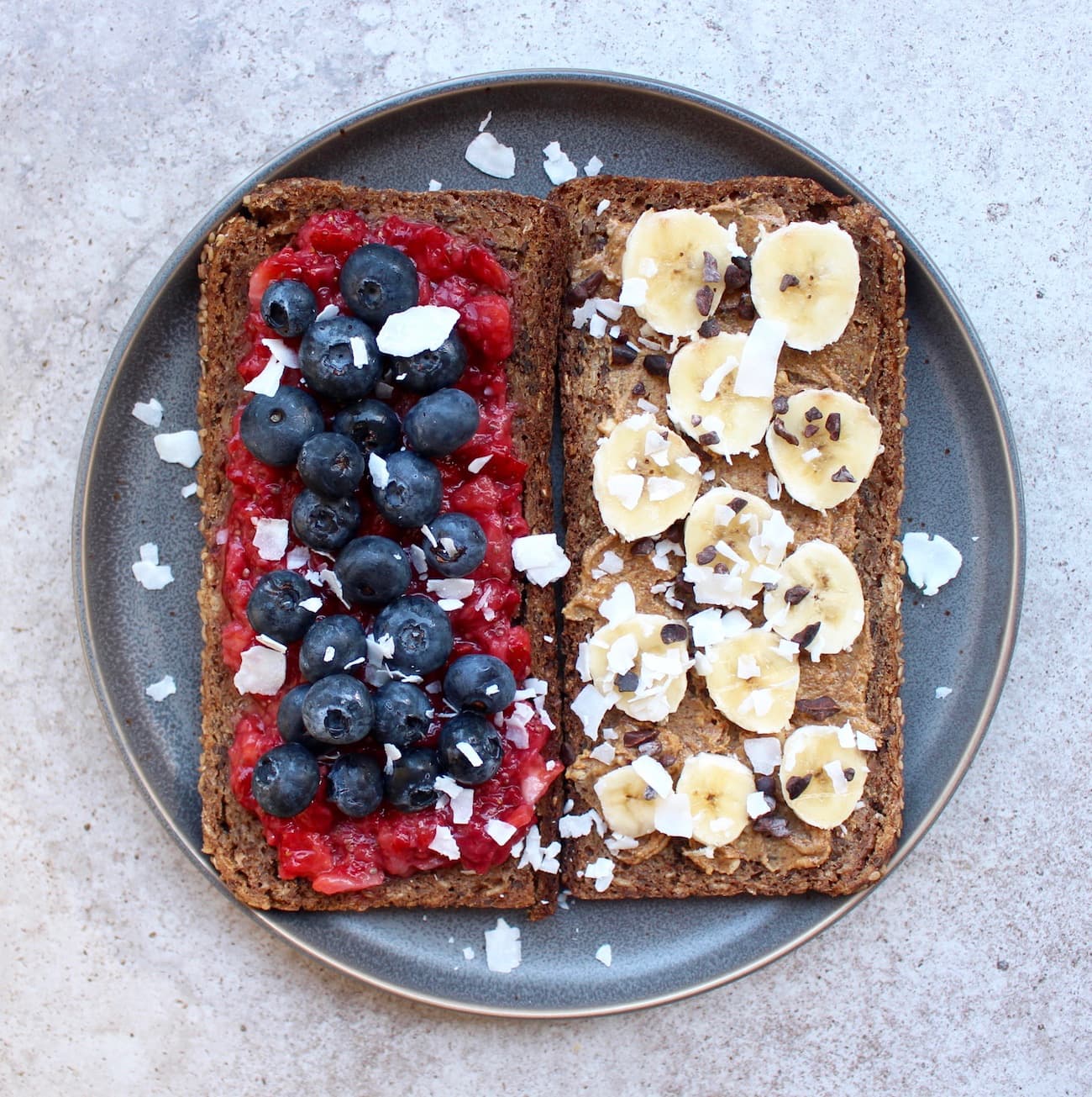 Toast topped with strawberry jam and blueberries and almond butter and banana
