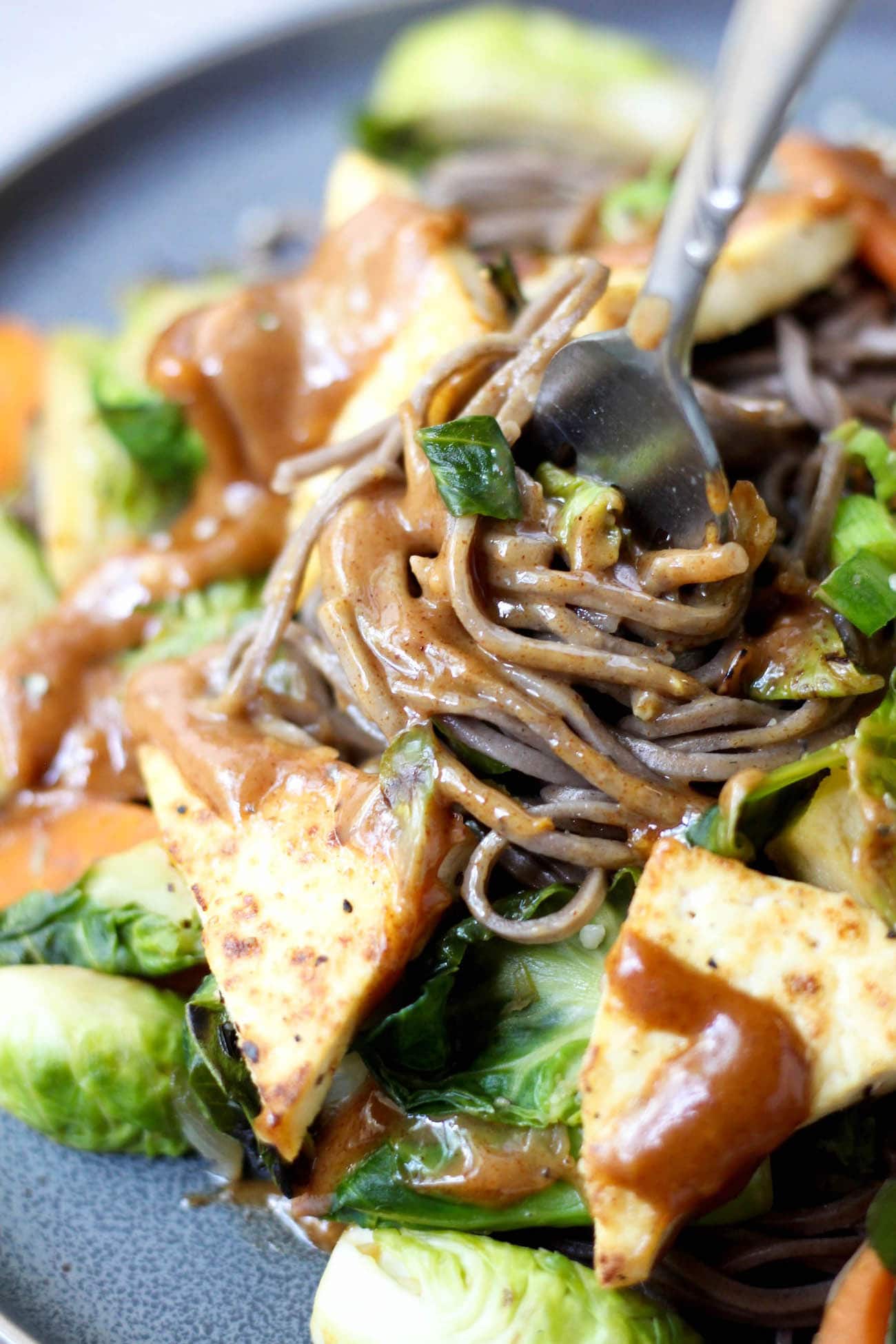 Vegan soba noodles with almond butter sauce being twirled onto a metal fork. 