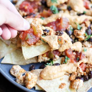 one vegan nacho being picked up from a plate of nachos