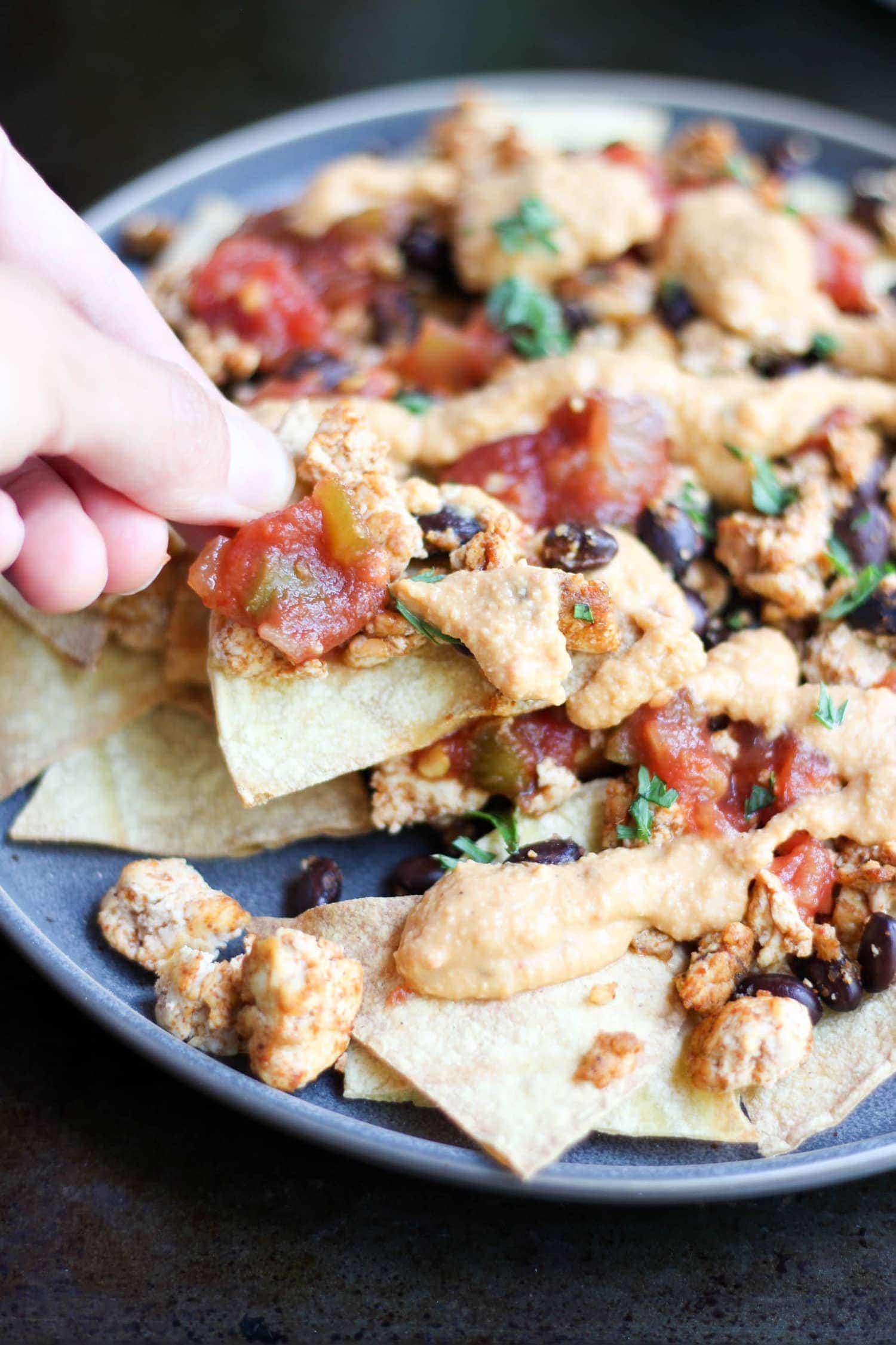 one vegan nacho being picked up from a plate of nachos