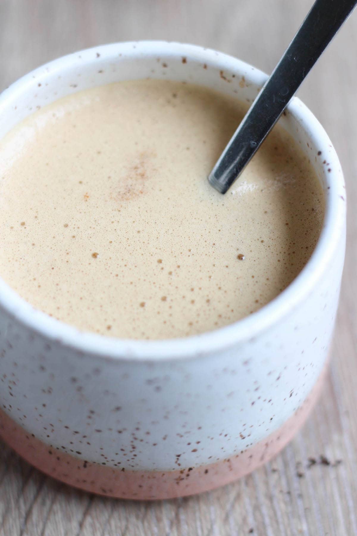 Frothy vegan bulletproof coffee in a white speckled mug with a metal spoon inside. 