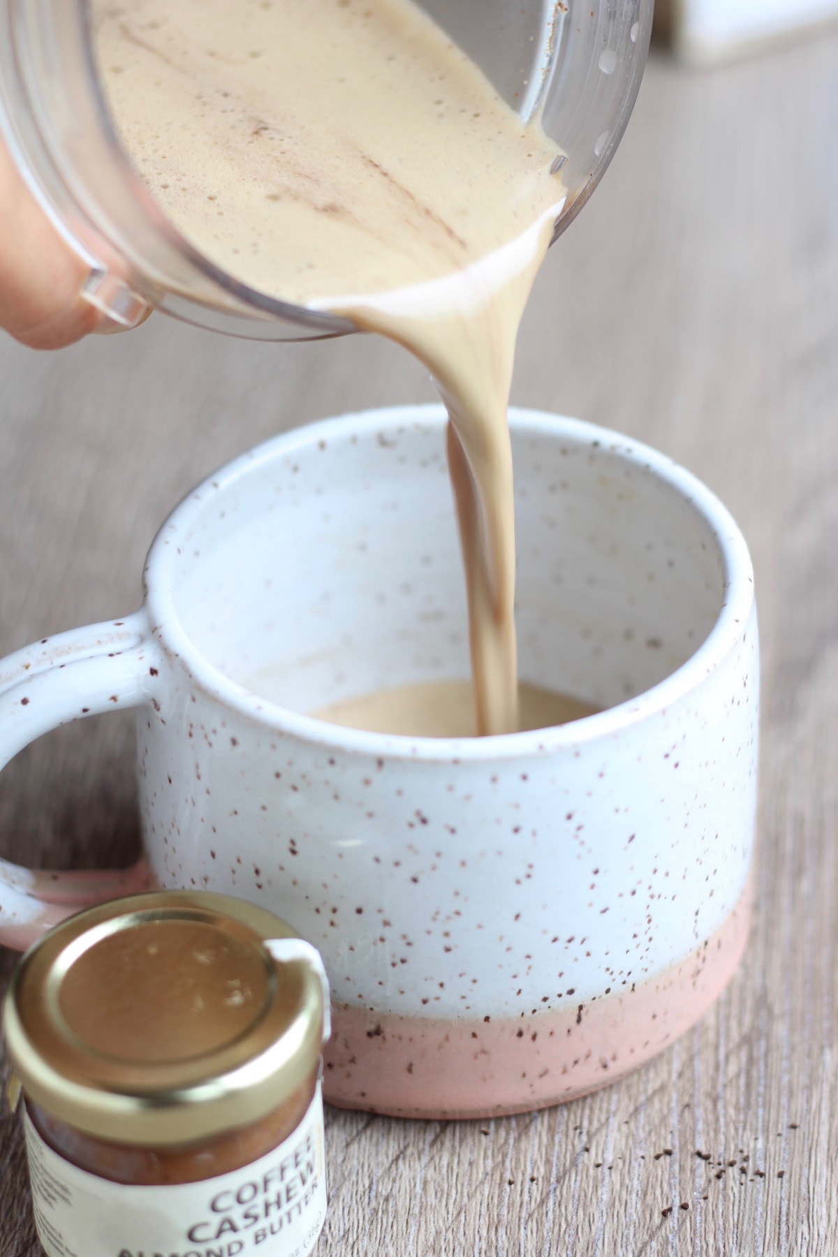 Frothy bulletproof coffee being poured into a white and pink speckled mug. 