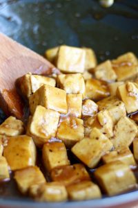 Orange tofu being stirred with wooden spoon in a pan