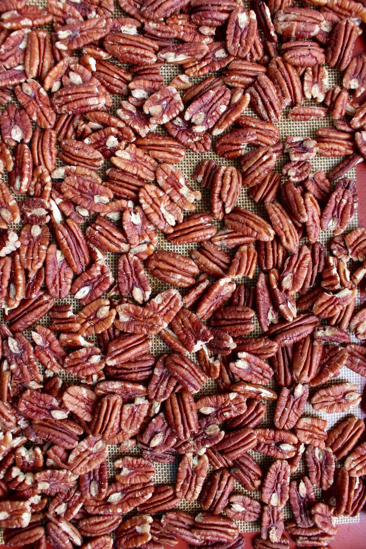 Raw pecans spread out to cover an entire baking sheet covered with a silicone baking mat. 