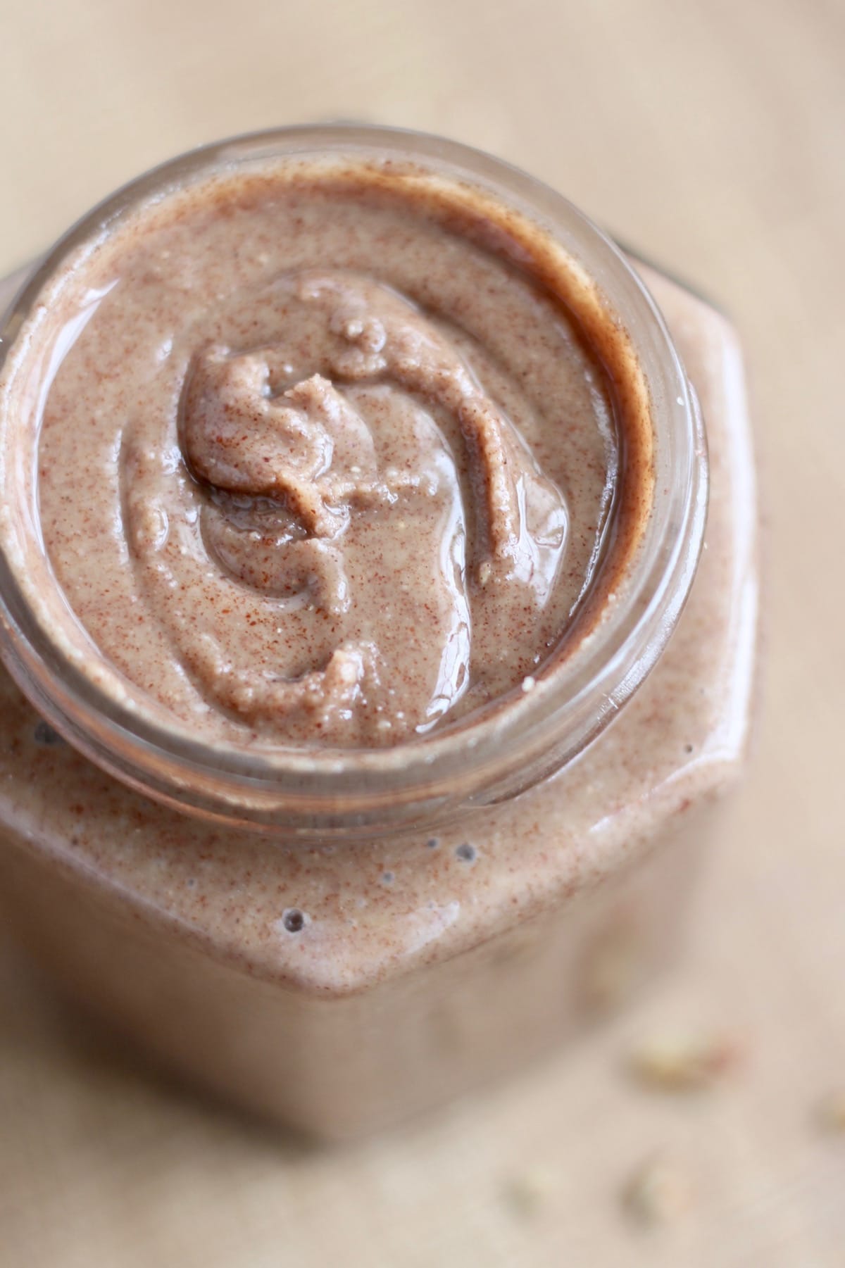 Brown homemade pecan butter in a glass jar with swirls in it. 