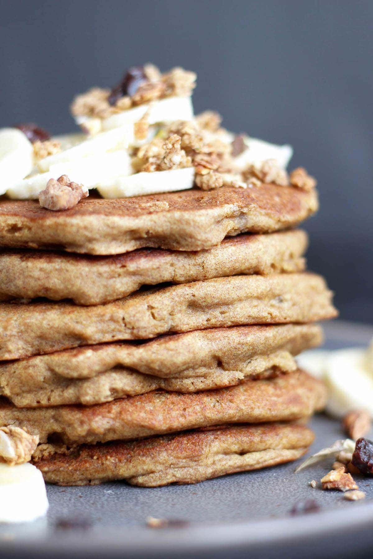 A tall stack of gluten free banana pancakes topped with banana and granola