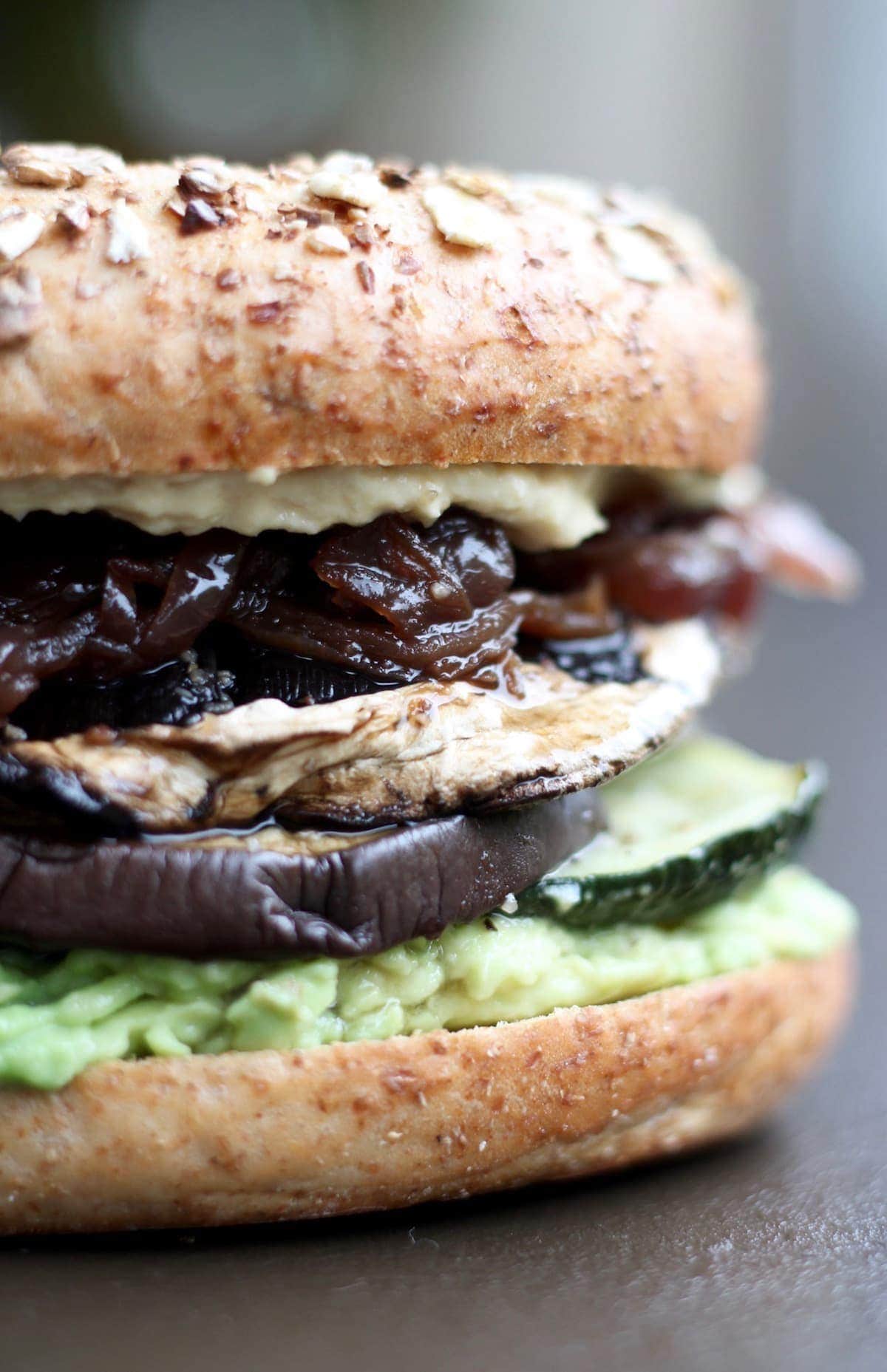 A toasted bagel stuffed with roasted veggies, hummus and veggies