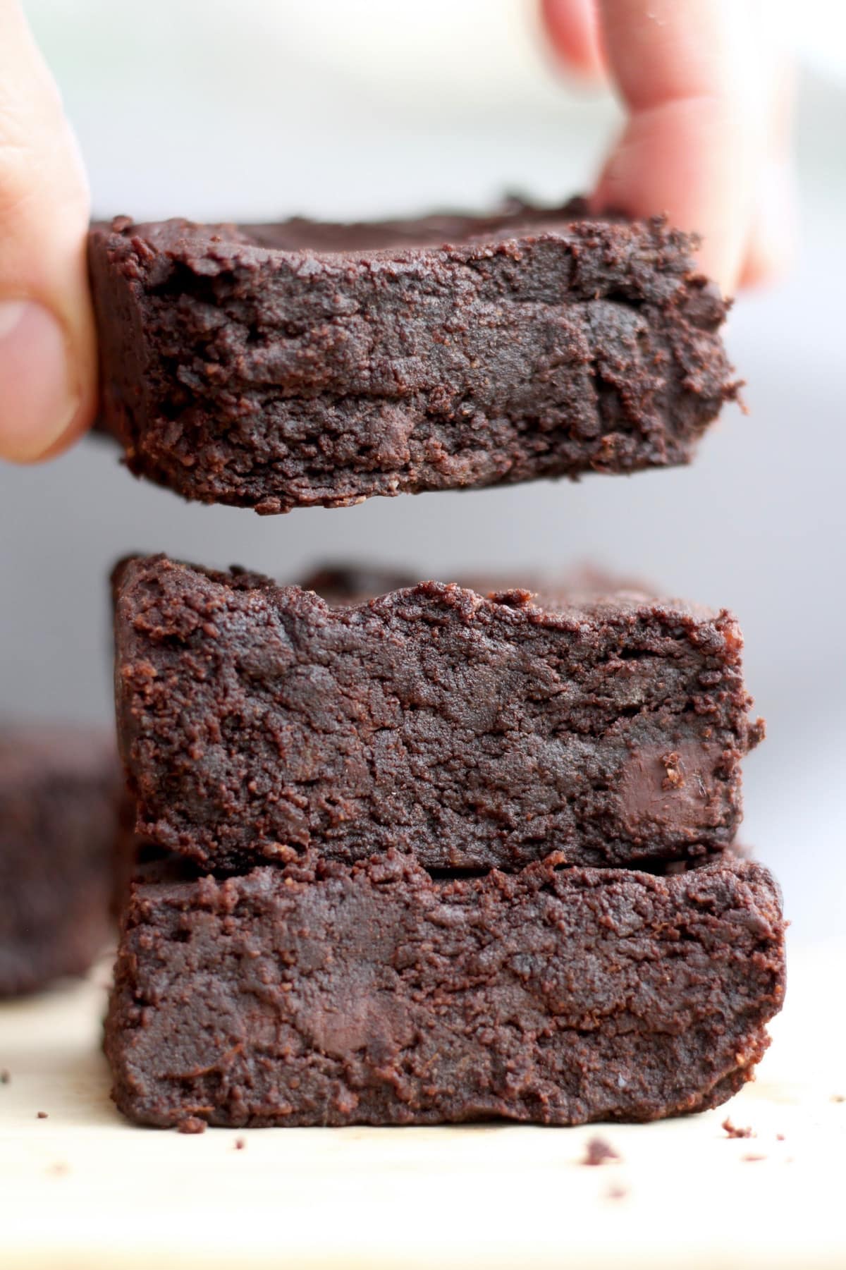 A hand taking the top brownie off a stack of three brownies.