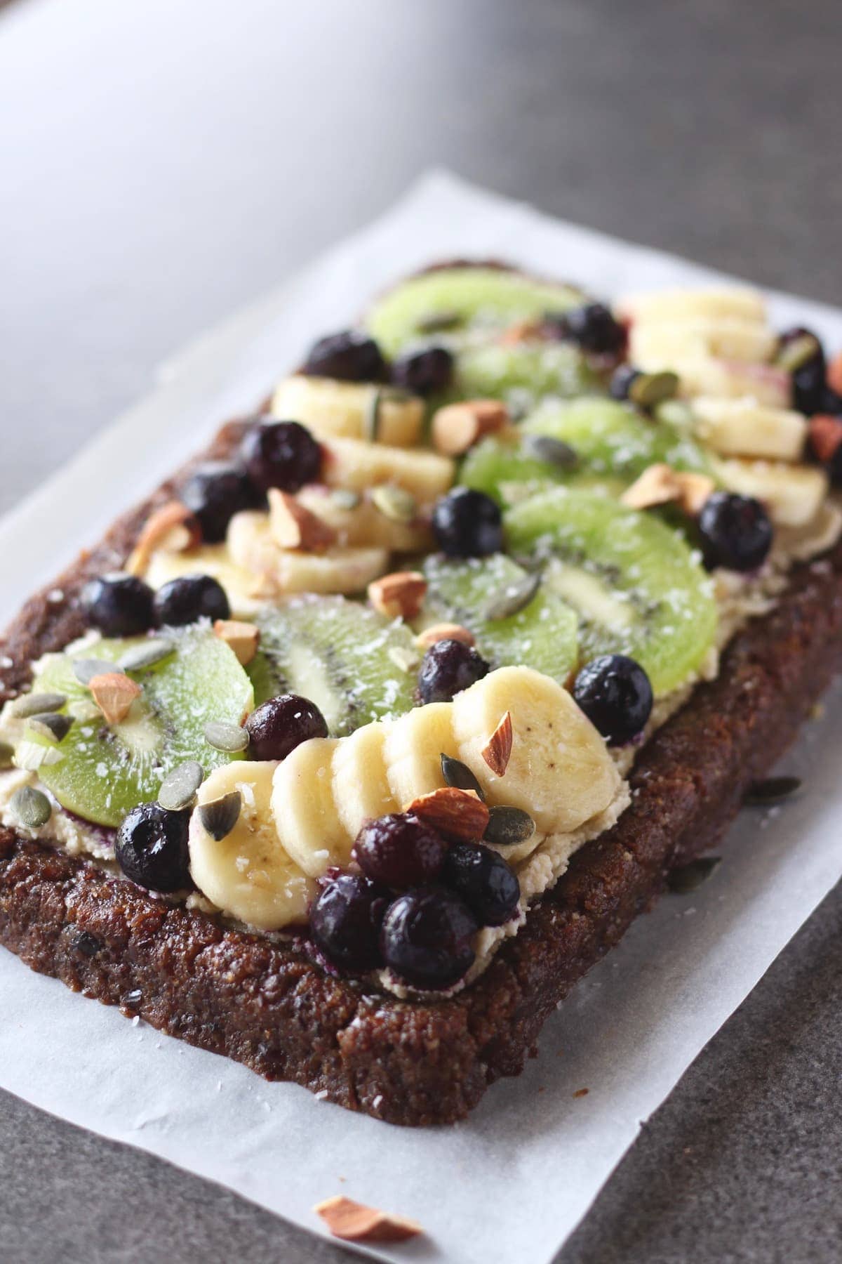 raw fruit pizza topped with banana, blueberries, kiwi and nuts and coconut