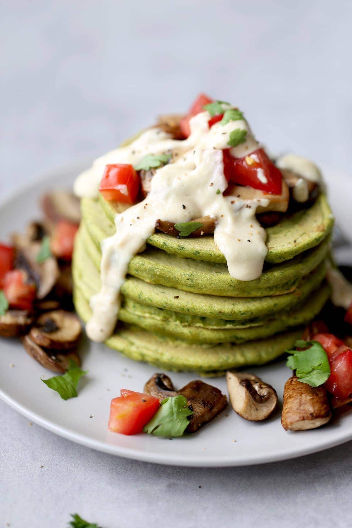 a stack of chickpea flour falafel pancakes topped with tahini sauce