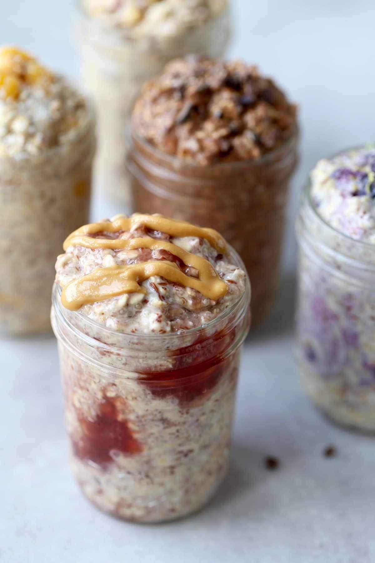 jar of peanut butter and jelly oats in a mason jar with 3 other overnight oat flavors in the background