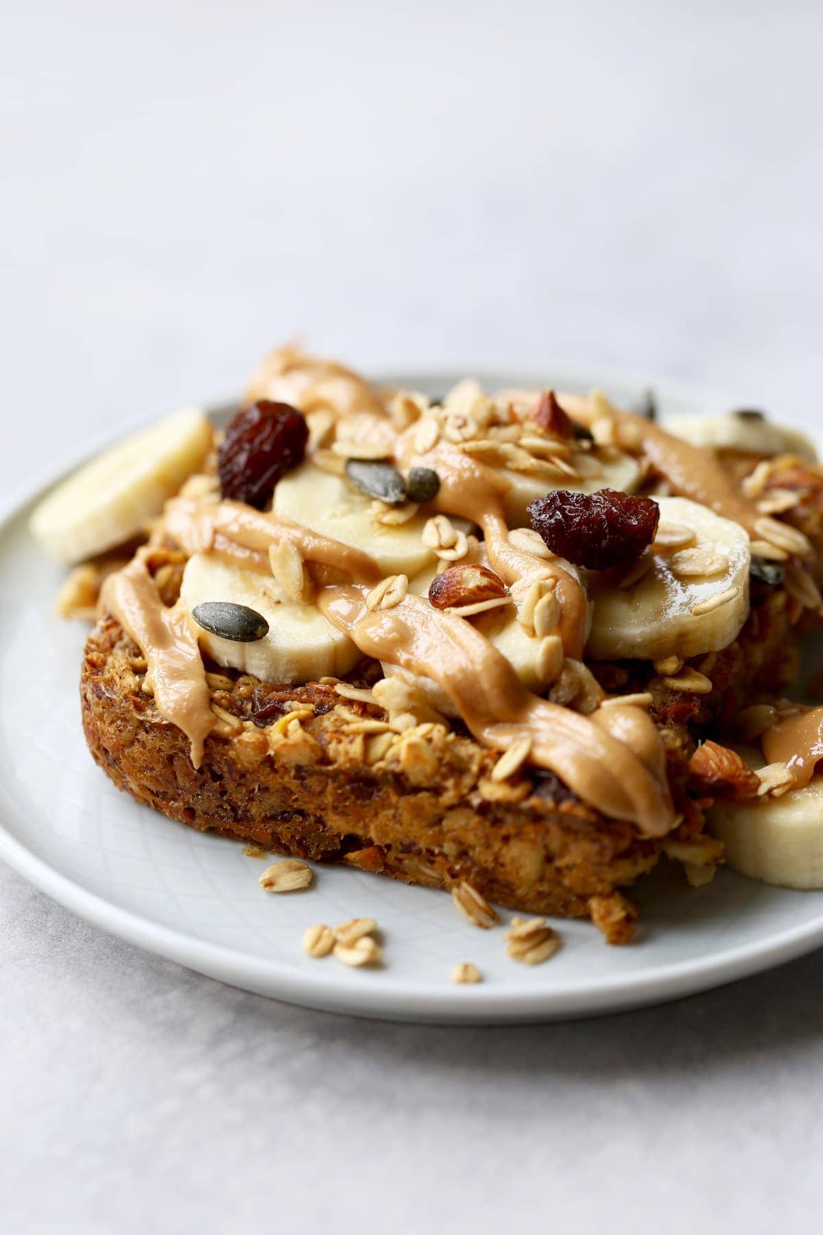 A thick slice of carrot cake baked oatmeal topped with banana slices, peanut butter and granola. 