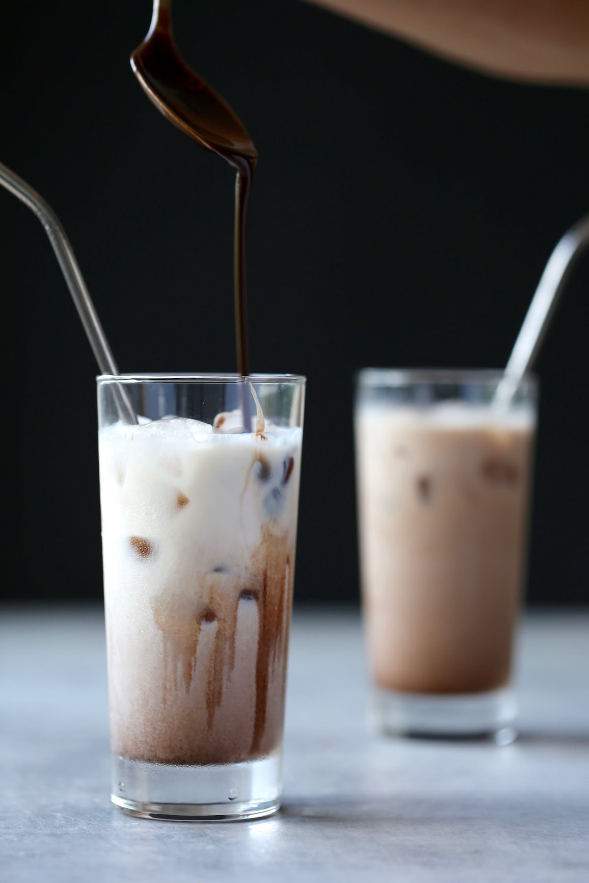 Homemade chocolate syrup being drizzled into a glass filled with milk and ice. 