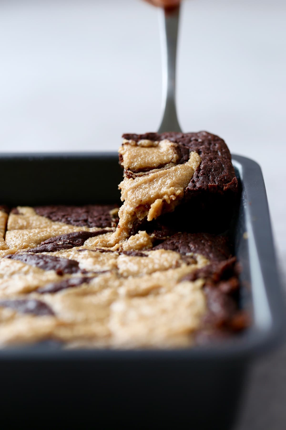 A fork lifting a peanut butter swirl brownie out of a metal baking dish. 
