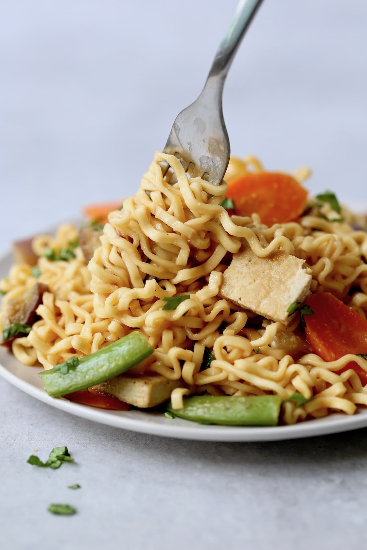 Miso ramen noodles twirled around a for with veggies and tofu nearby. 