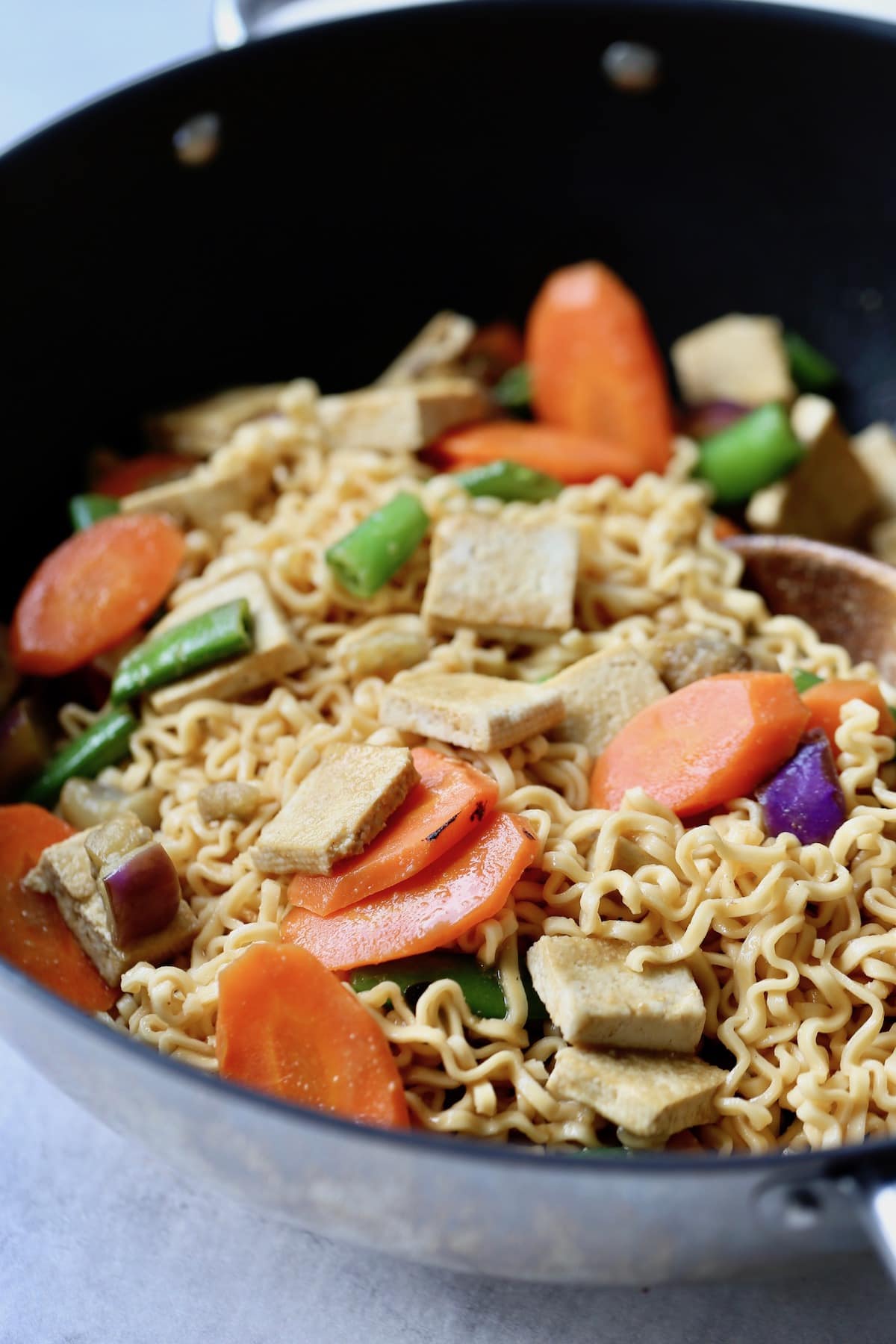 Miso noodles, carrots, purple cabbage, green beans and tofu stirred together in a large black wok.