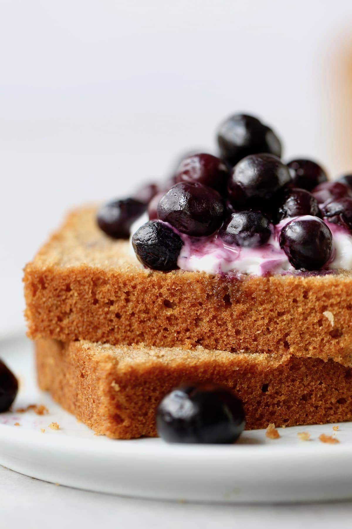 2 slices of Whole Wheat Olive Oil Tea Cake topped with blueberries on a plate