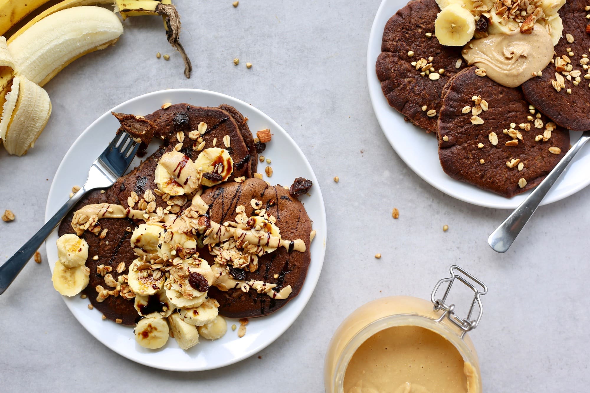 plates of chocolate chickpea flour pancakes loaded with nut butter, banana, and granola