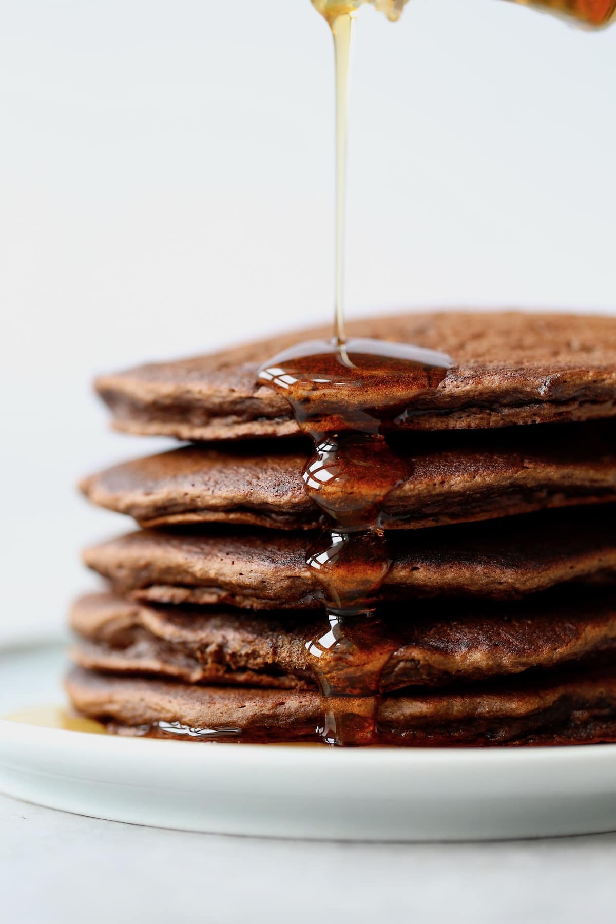 maple syrup being poured over a stack of chocolate pancakes