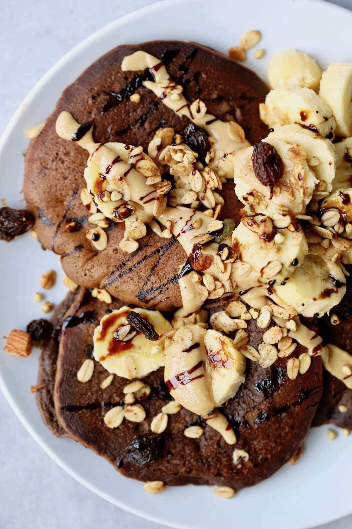 chocolate chickpea flour pancakes topped with banana, peanut butter and granola