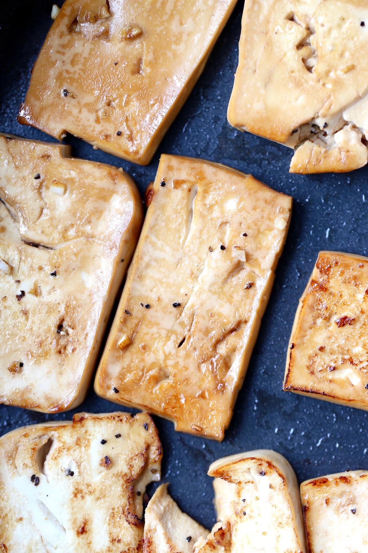 Rectangles of marinated tofu browning on a black skillet. 