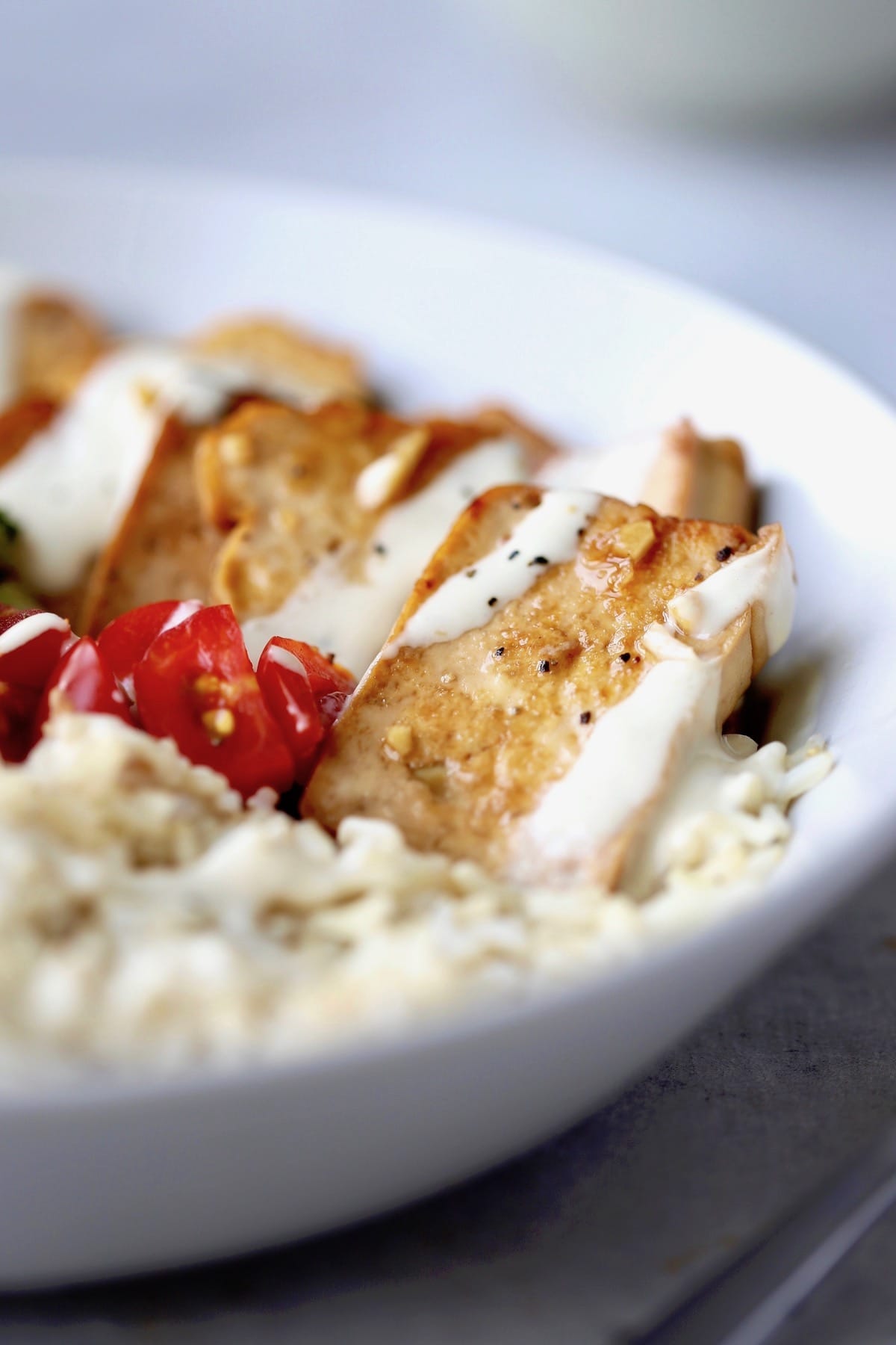 Marinated, fried tofu on rice drizzled with tahini sauce and sprinkled with black pepper. 