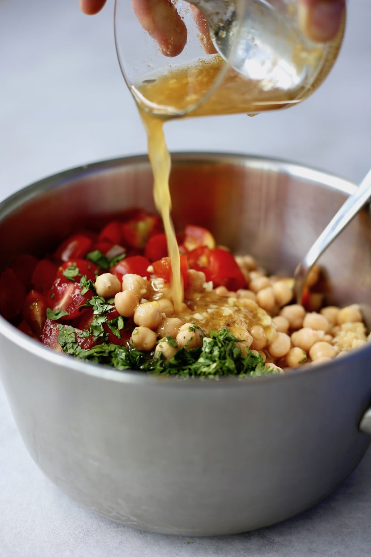 lemon dressing being poured over a mixture of quinoa, chickpeas, tomatoes and cilantro