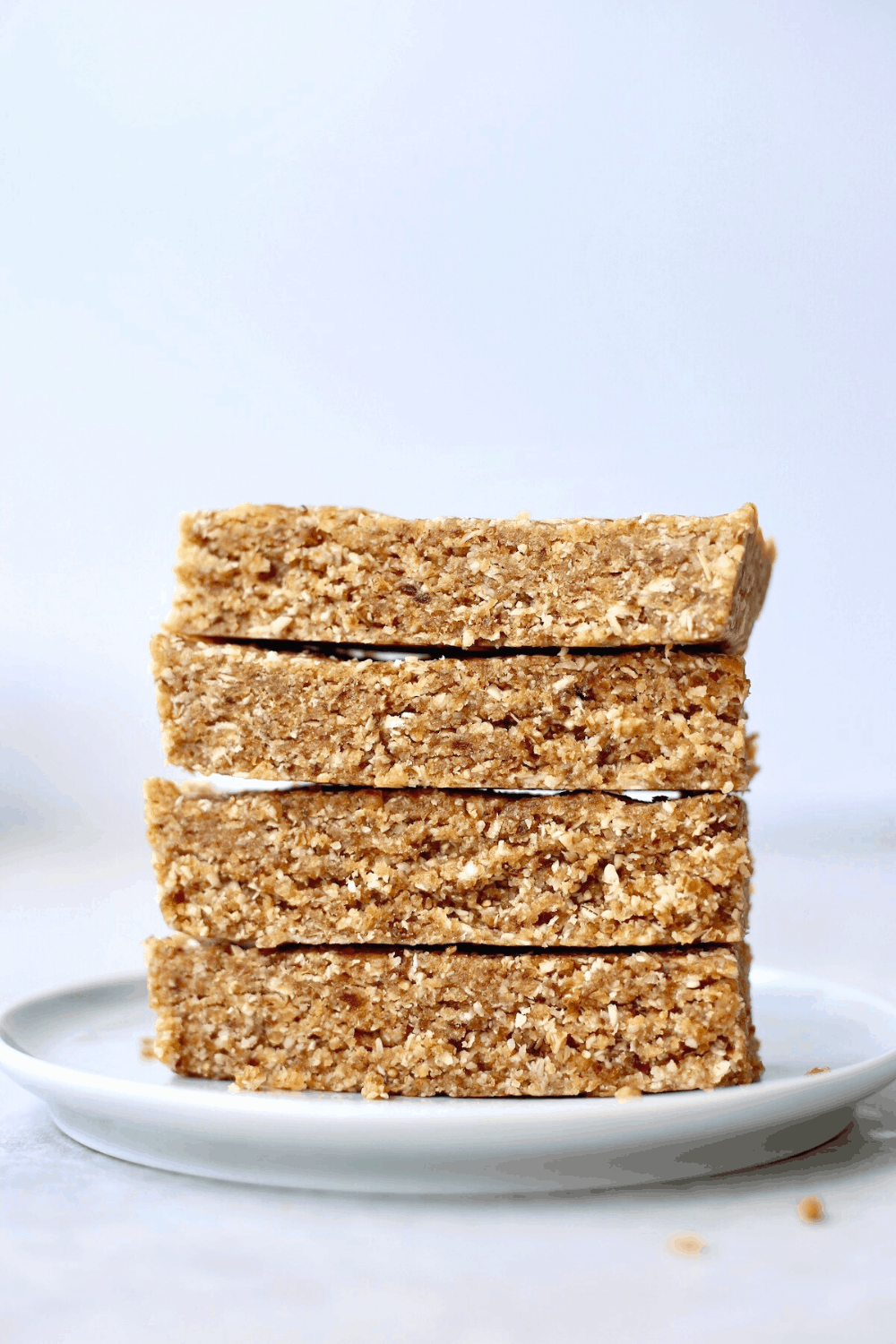 A side view of four golden brown rectangular homemade granola bars stacked on a light blue plate.